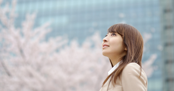 桜の木を背景に空を見上げるスーツの女性